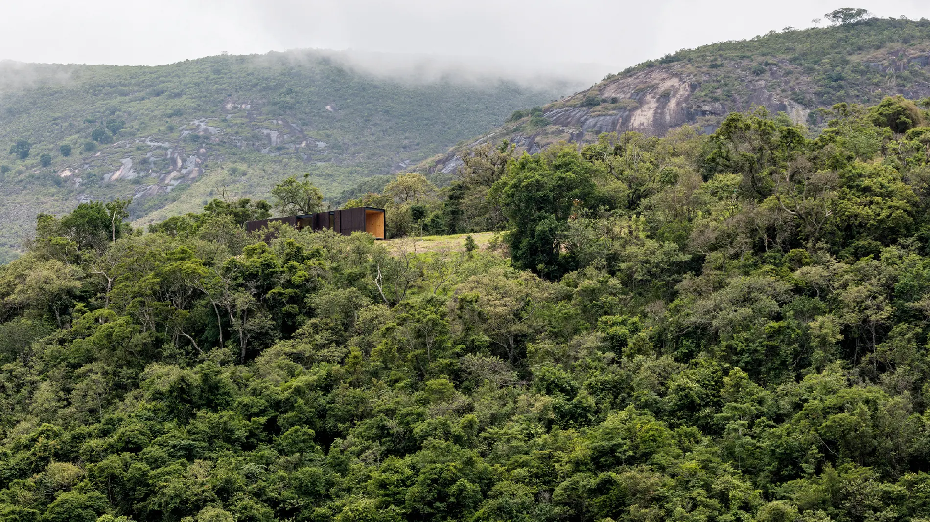 A low dark cabin above a wooded hillside